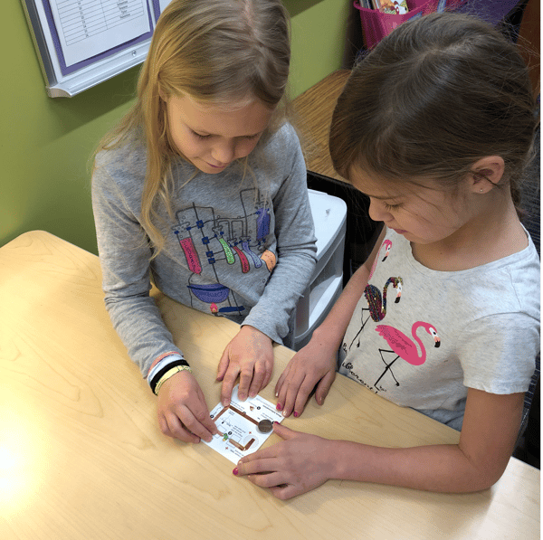 two second grade girls making a paper circuit