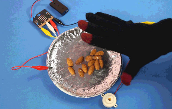 Electro Fingers glove connected to a micro:bit moving over a metal plate with almonds.